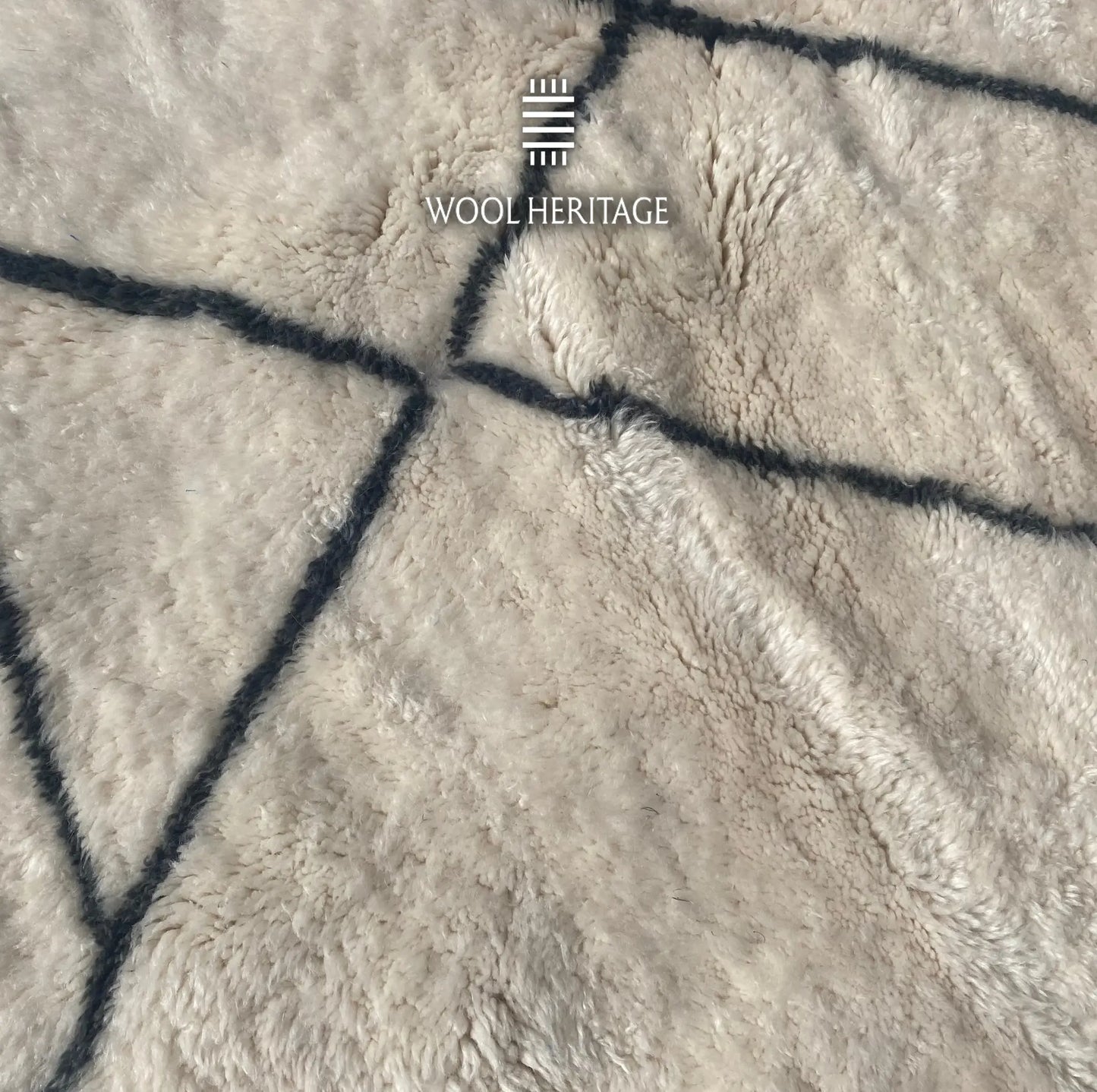 Detailed view of ADRAR rug showing intersecting charcoal mountain-like lines against the soft ivory wool pile