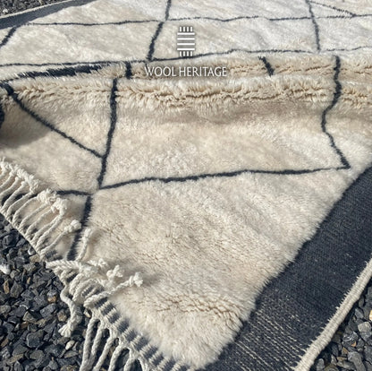 Folded detail of ADRAR hand-knotted rug showing its ivory wool pile, charcoal linework, side border, and fringe