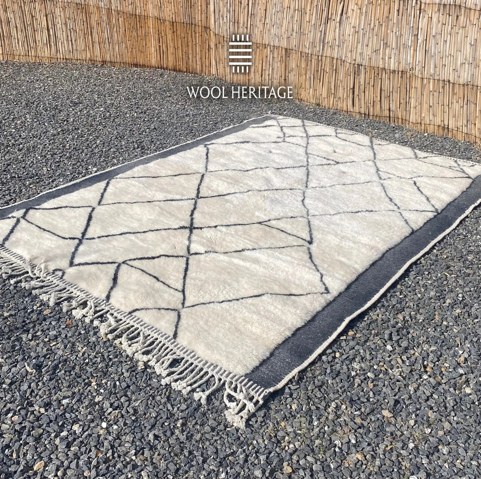 Angled view of ADRAR Moroccan wool rug showing its irregular mountain pattern, charcoal borders, and cotton fringe