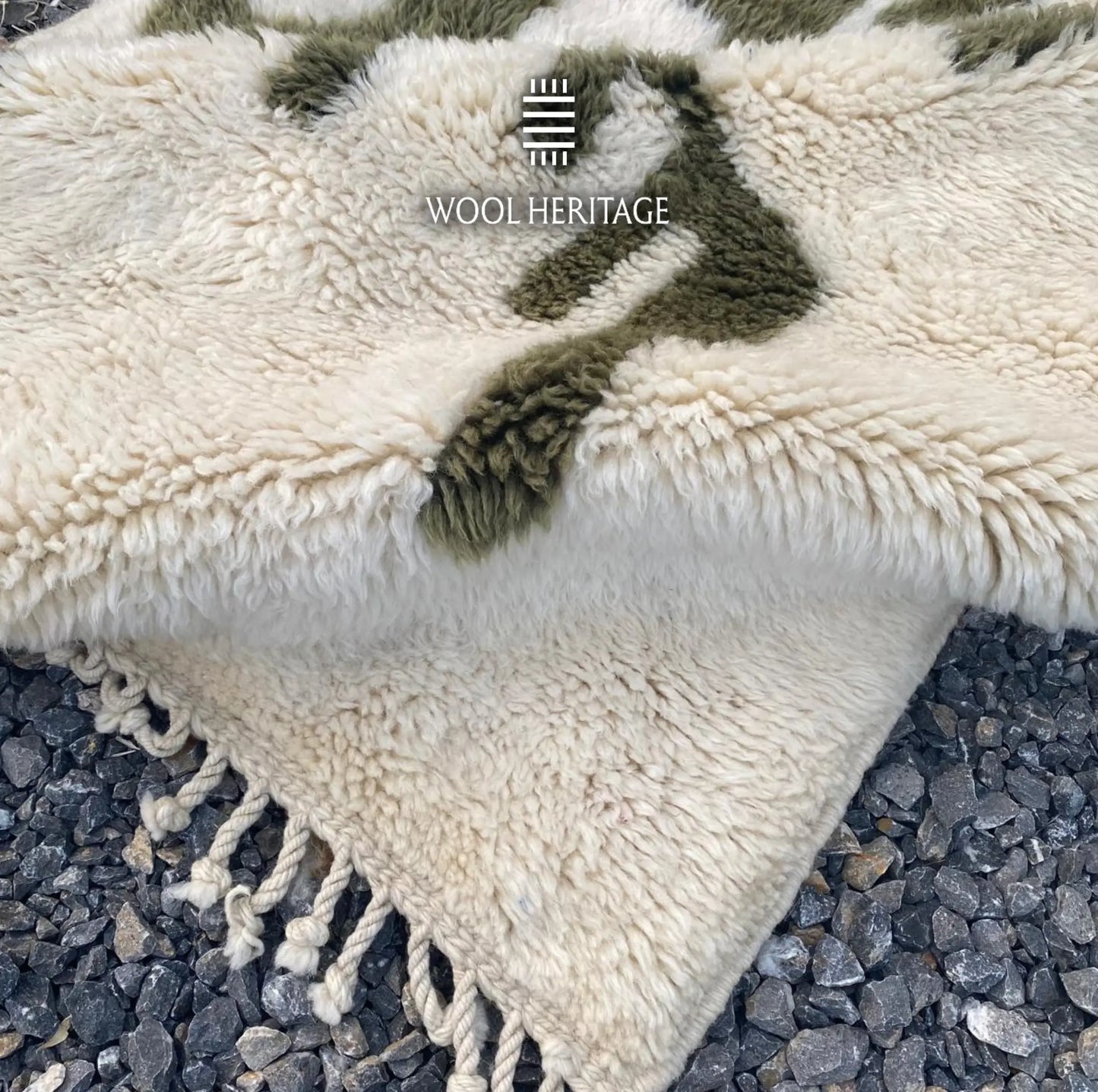Folded detail of AKNARI hand-knotted rug showing its thick ivory pile, olive design, and cotton fringe