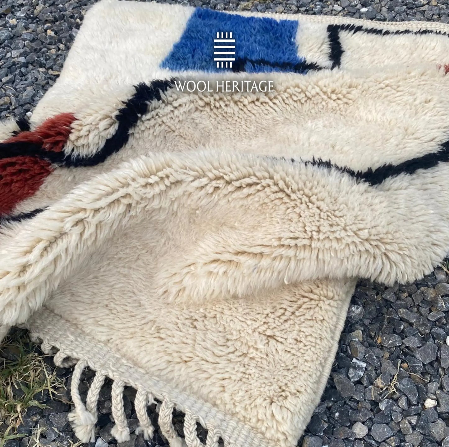 Folded AMARG hand-knotted rug showing its thick ivory pile, blue and burgundy accents, and cotton fringe