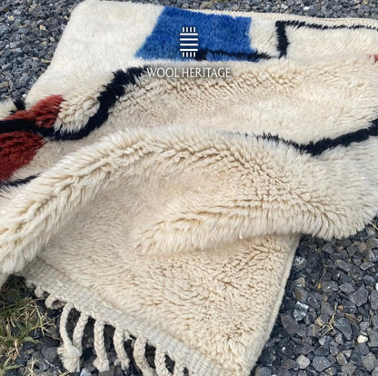Folded AMARG hand-knotted rug showing its thick ivory pile, blue and burgundy accents, and cotton fringe