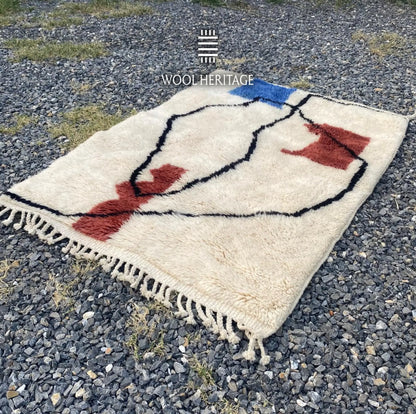 Angled view of AMARG Moroccan wool rug showing its flowing black lines, burgundy forms, and hand-finished fringe