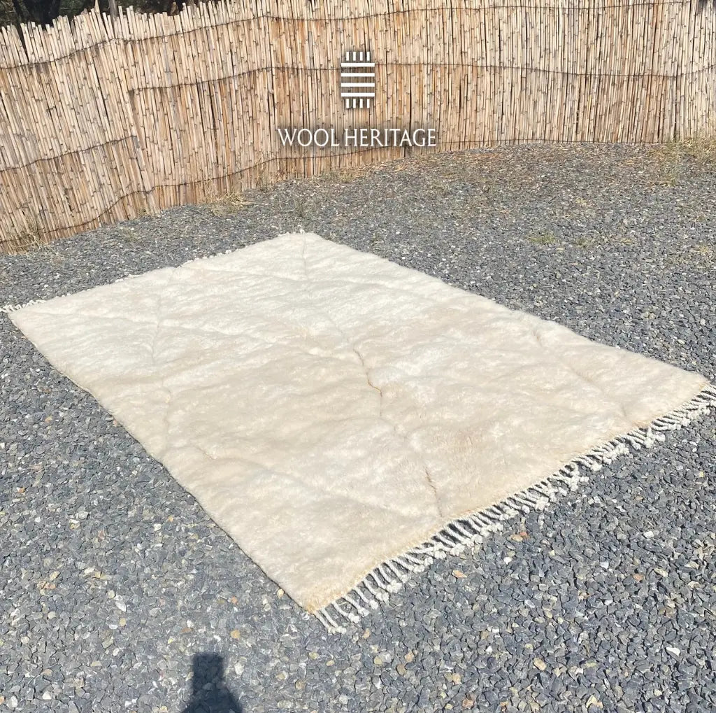 Angled view of AMLAL Beni Mrirt rug laid flat, showing its subtle ivory geometric lines and soft wool surface