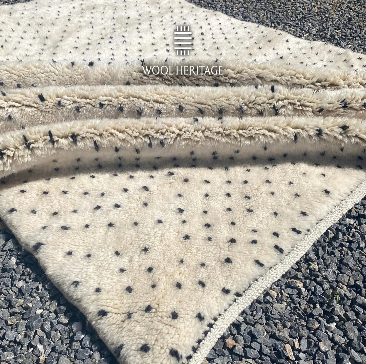 Folded detail of AMUD hand-knotted rug showing its thick ivory pile, charcoal dotted pattern, and finished edges