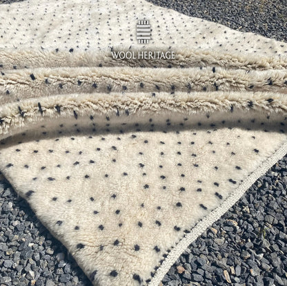 Folded detail of AMUD hand-knotted rug showing its thick ivory pile, charcoal dotted pattern, and finished edges