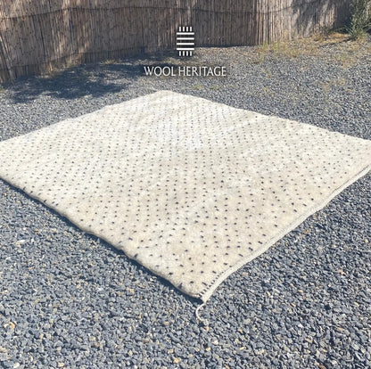 Angled view of AMUD Moroccan wool rug showing its scattered charcoal seed pattern and hand-finished edges