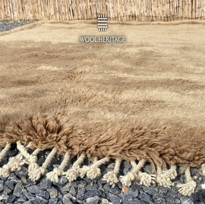 Close-up of ASIREM camel wool rug showing its soft pile, raised border, and hand-plaited fringe