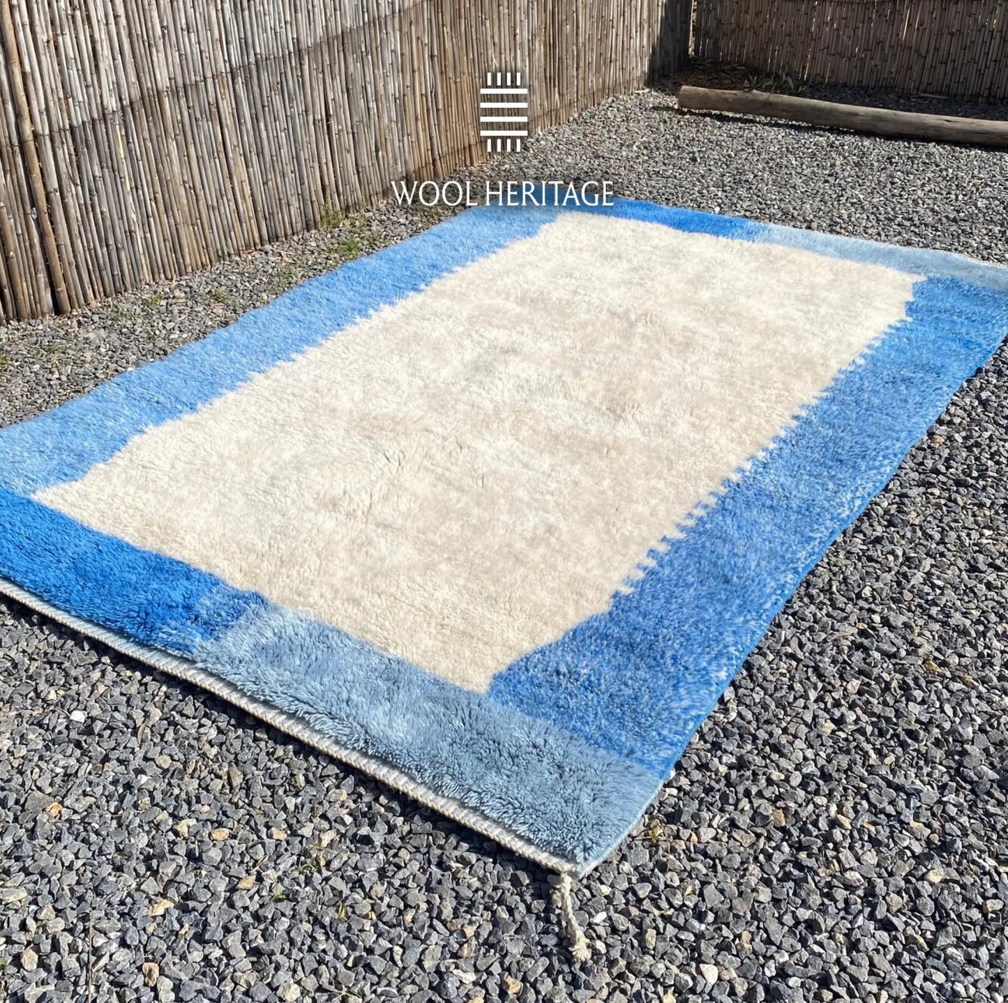 Angled view of IGENNA Moroccan wool rug showing its ivory field, irregular blue border, and hand-finished edges