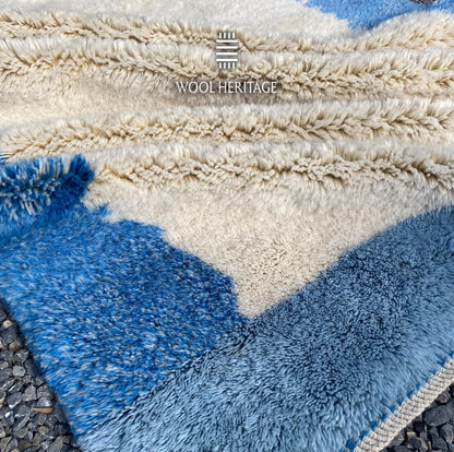 Folded detail of IGENNA hand-knotted rug showing its thick ivory pile and layered pale and deep blue colour fields