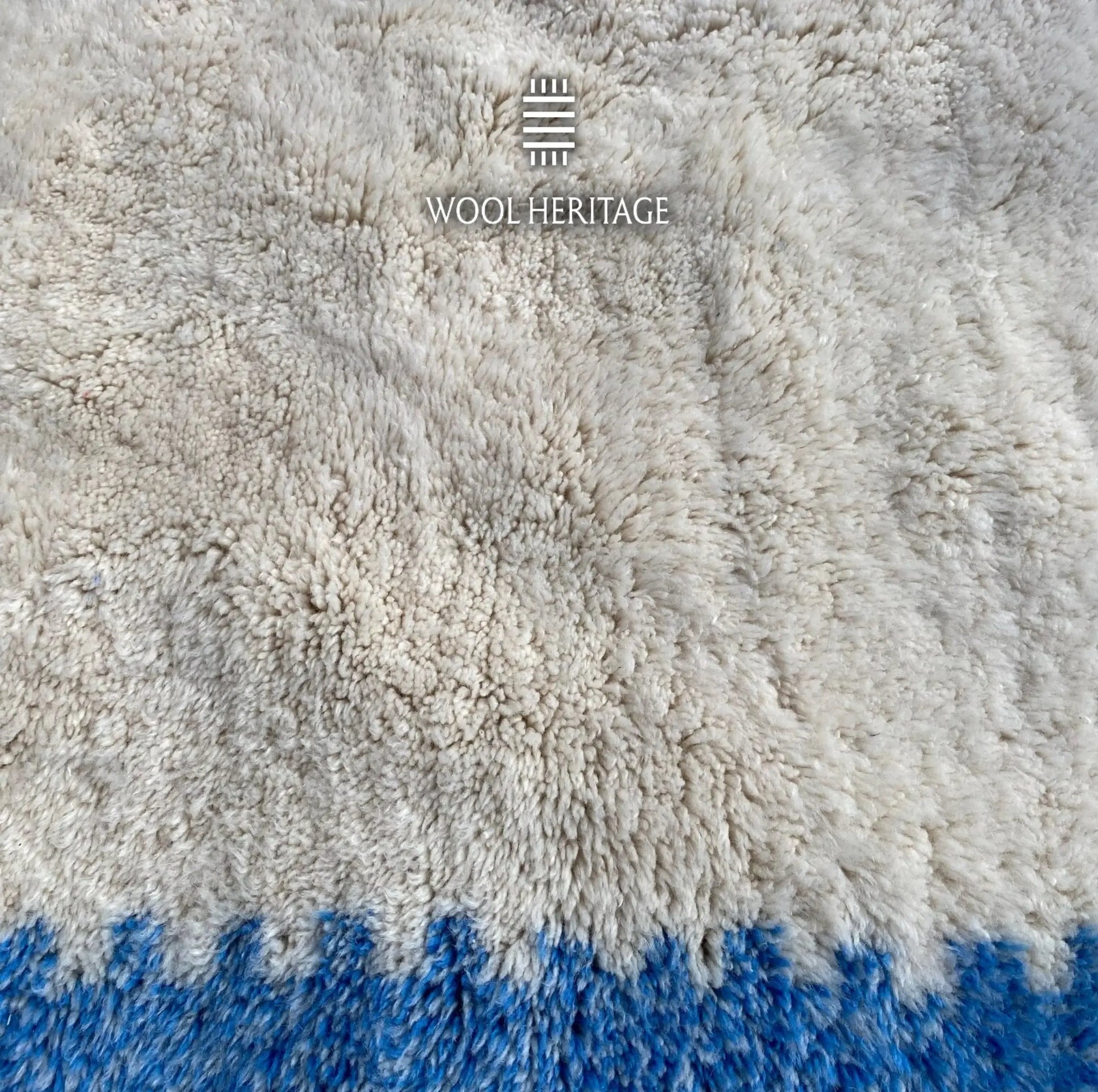 Detailed view of IGENNA rug showing the dense soft ivory Moroccan wool pile beside a blue border