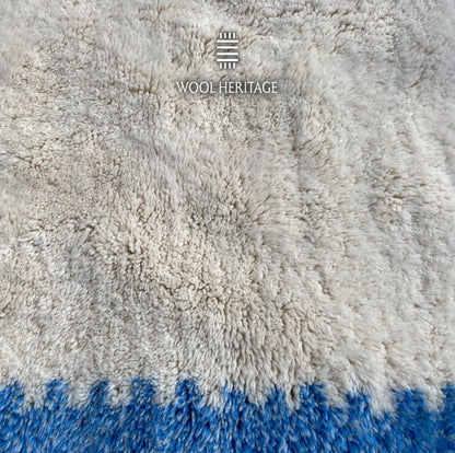 Detailed view of IGENNA rug showing the dense soft ivory Moroccan wool pile beside a blue border