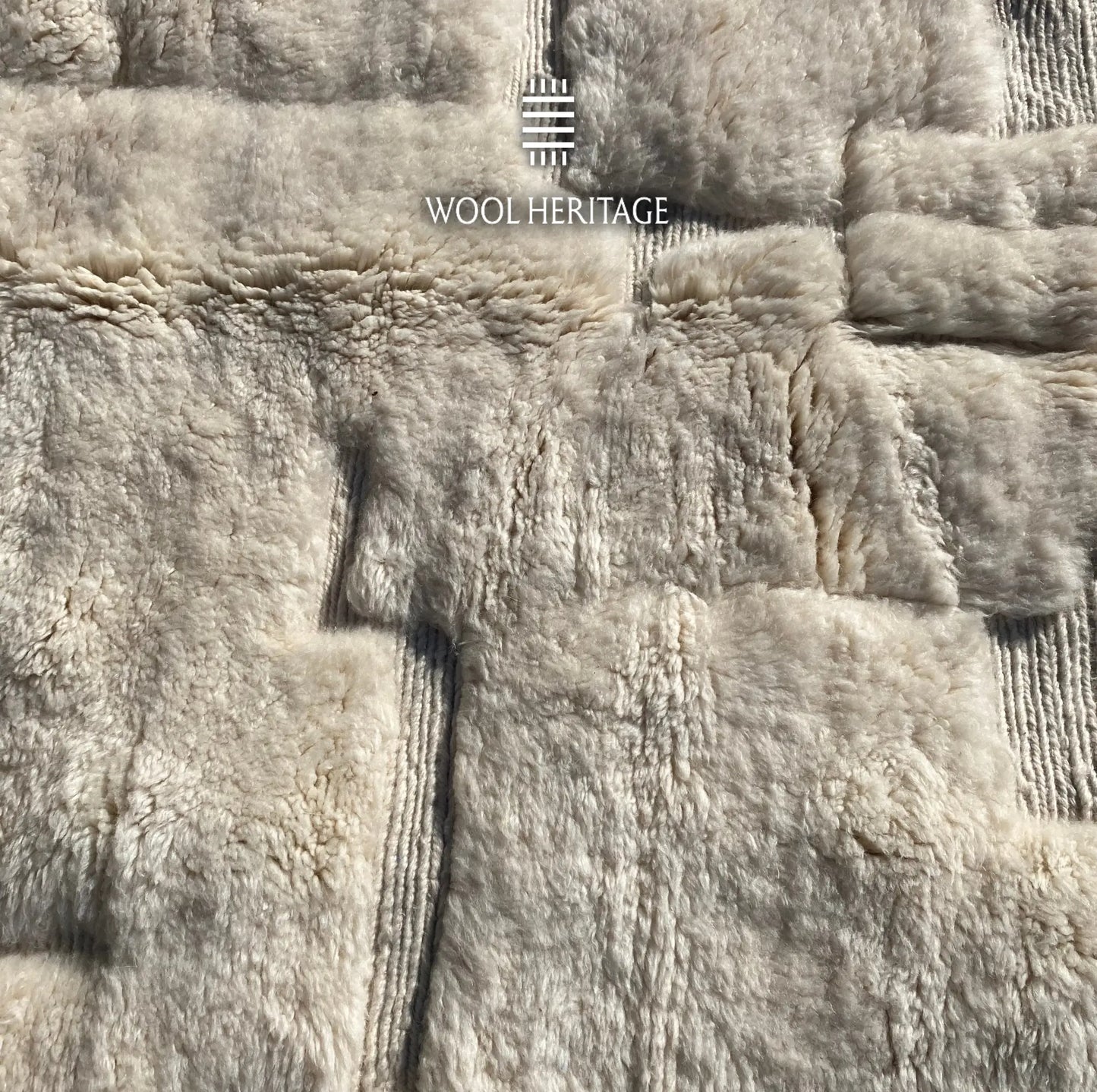 Close-up of IGHREM ivory rug showing its raised blocks, recessed lines, and varied wool texture