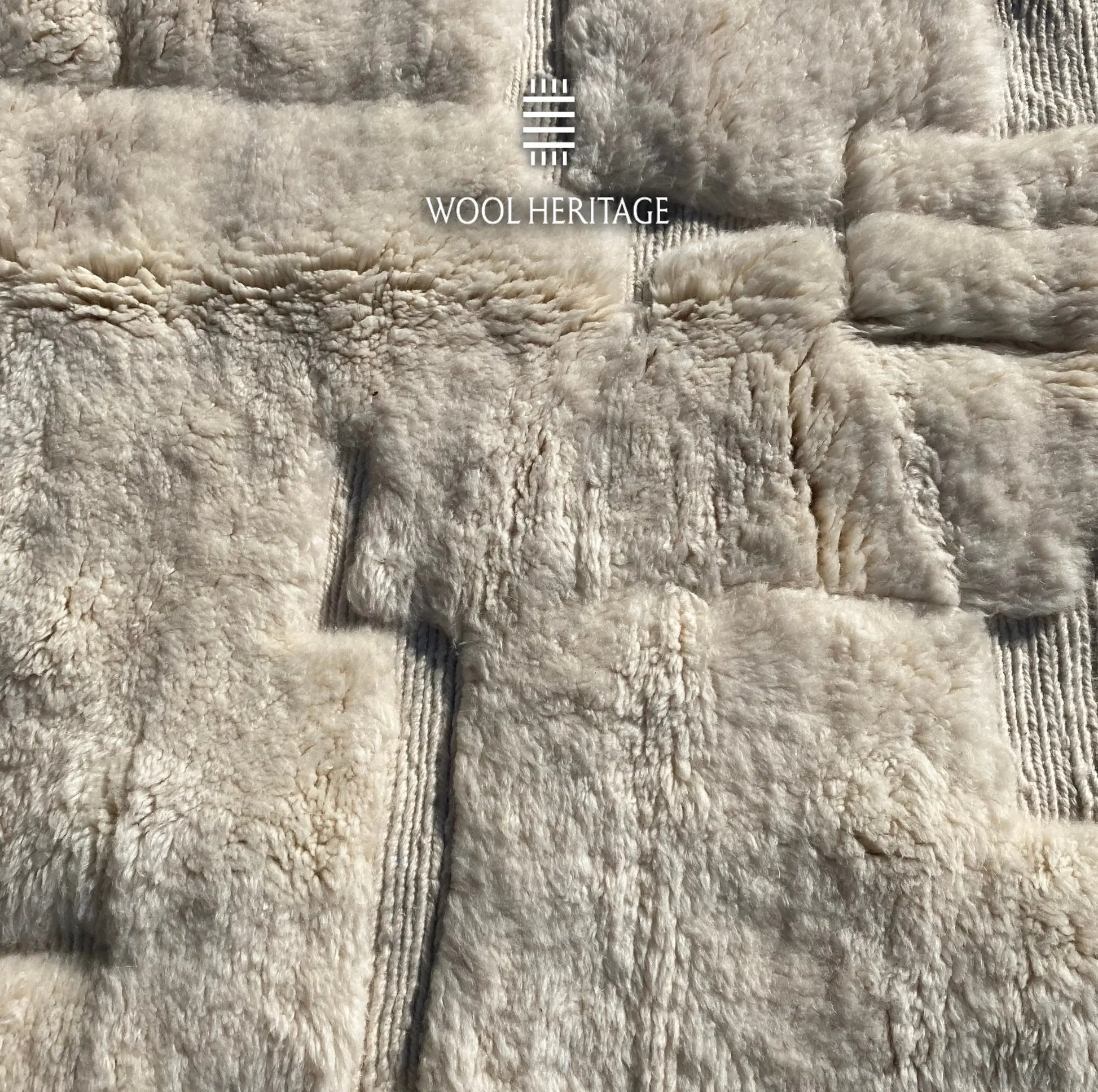 Close-up of IGHREM ivory rug showing its raised blocks, recessed lines, and varied wool texture