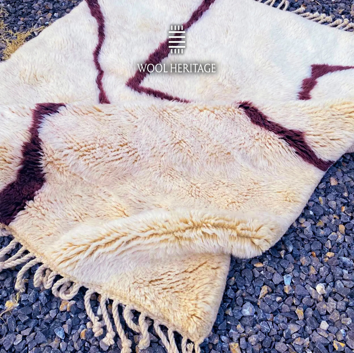 Folded detail of IZURAN hand-knotted rug showing its thick ivory wool pile, burgundy linework, and hand-finished fringe