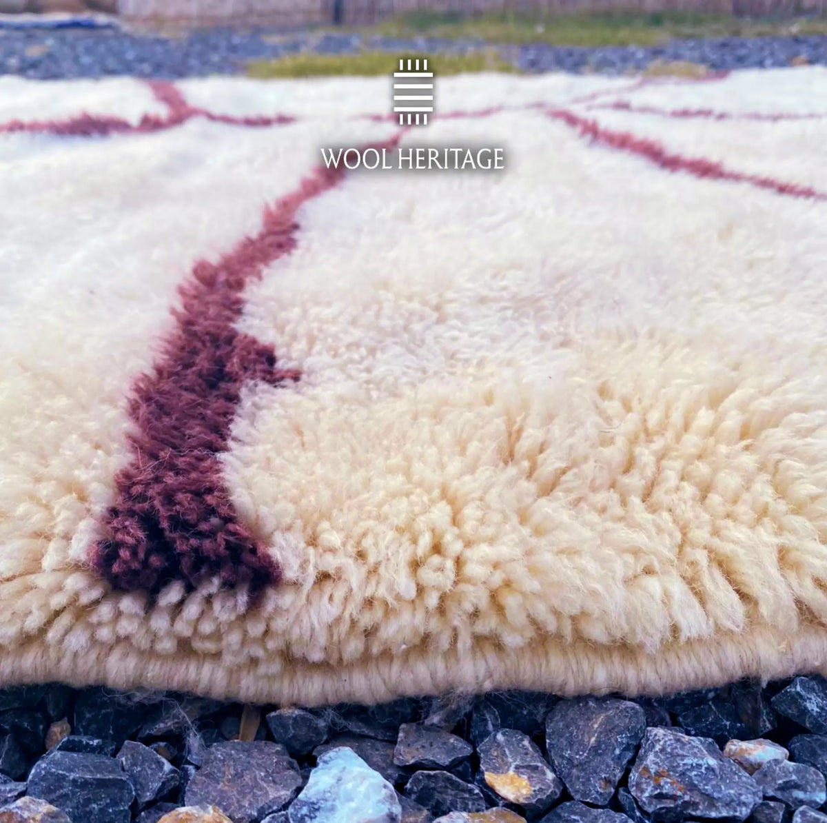 Close-up of IZURAN rug showing its soft ivory Moroccan wool pile and raised deep burgundy root-like line