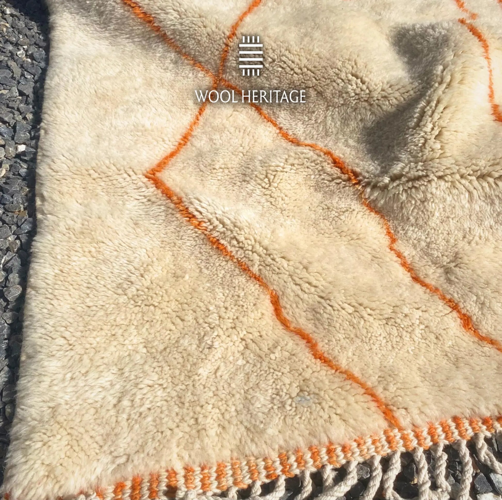 Folded detail of TAFUKT hand-knotted rug showing its thick ivory wool pile and warm orange geometric lines