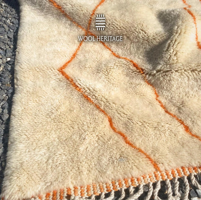 Folded detail of TAFUKT hand-knotted rug showing its thick ivory wool pile and warm orange geometric lines