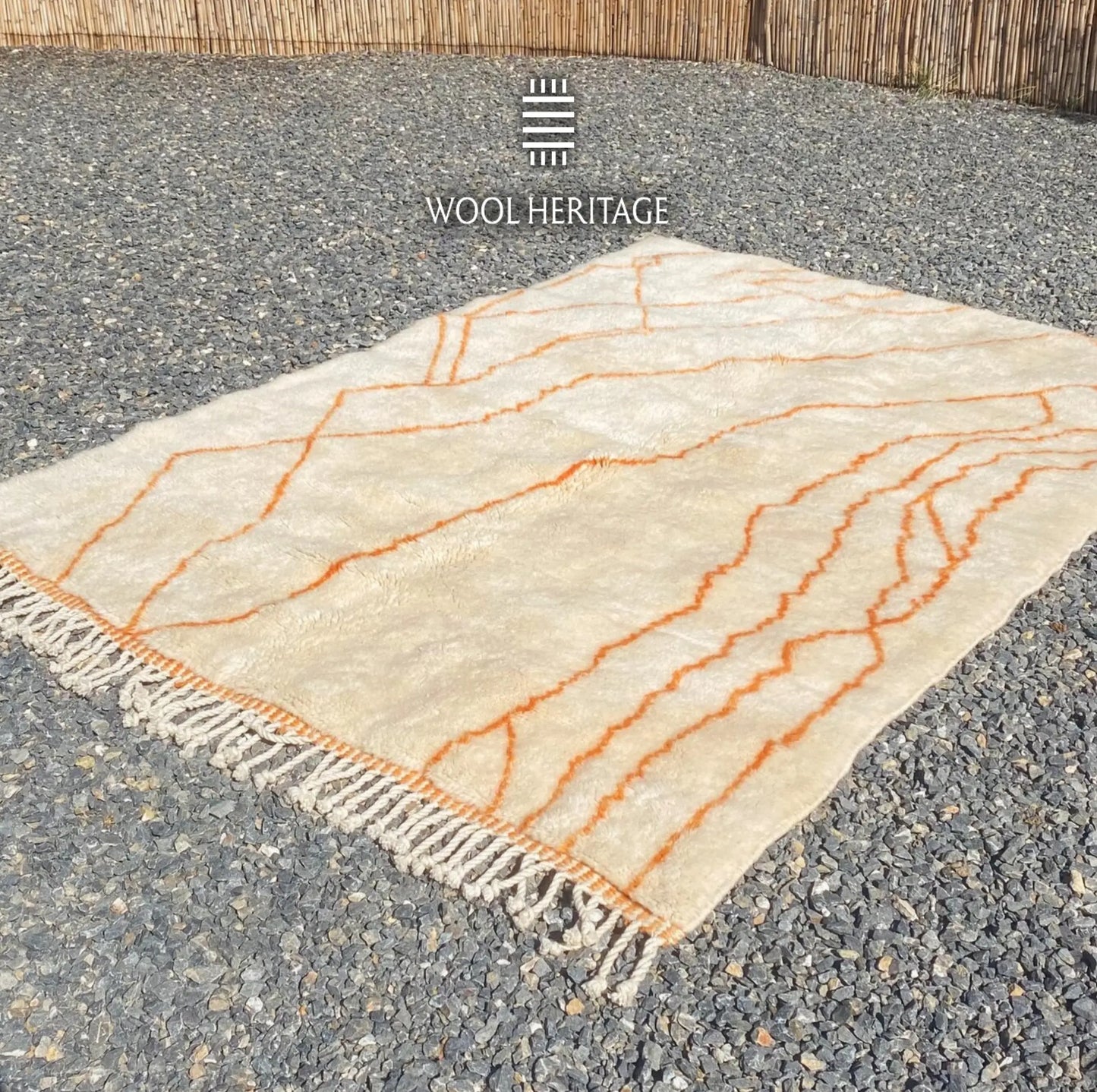 Angled view of TAFUKT Moroccan wool rug showing its flowing orange linework and hand-finished fringe