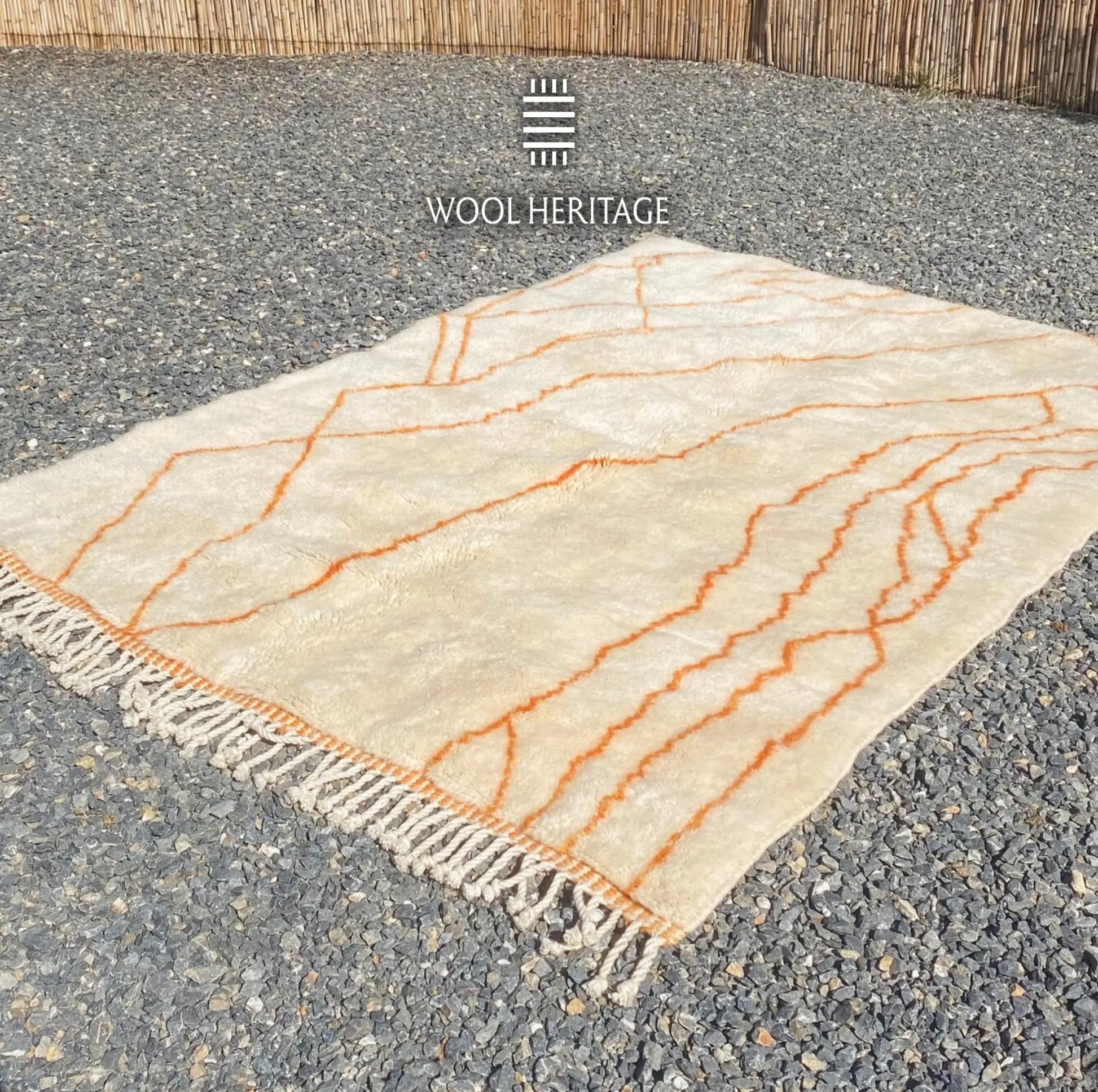 Angled view of TAFUKT Moroccan wool rug showing its flowing orange linework and hand-finished fringe