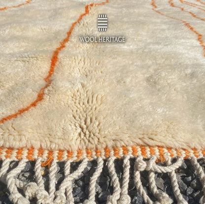 Close-up of TAFUKT rug showing its soft ivory Moroccan wool pile, orange linework, finished edge, and fringe