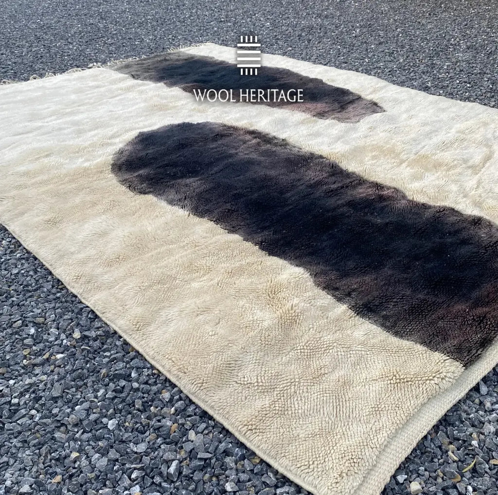 Angled view of TAFUNAST Moroccan rug showing its bold charcoal forms, ivory wool field, and hand-finished fringe
