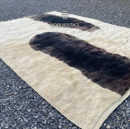 Angled view of TAFUNAST Moroccan rug showing its bold charcoal forms, ivory wool field, and hand-finished fringe