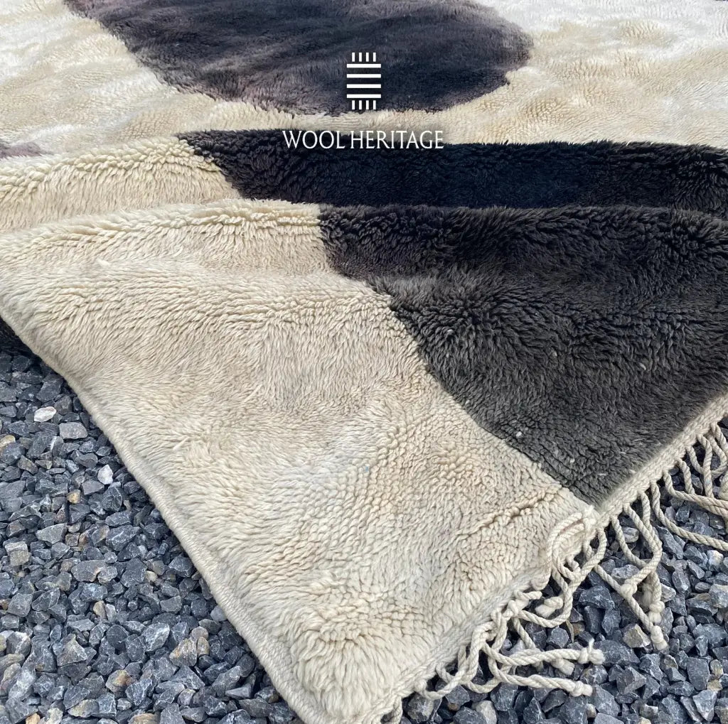 Detail of TAFUNAST hand-knotted rug showing a charcoal cattle-inspired form, ivory pile, and fringe finish