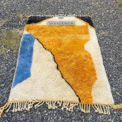 TAMURT abstract Moroccan wool rug laid flat, showing its flowing golden ochre, ivory, navy, and blue design