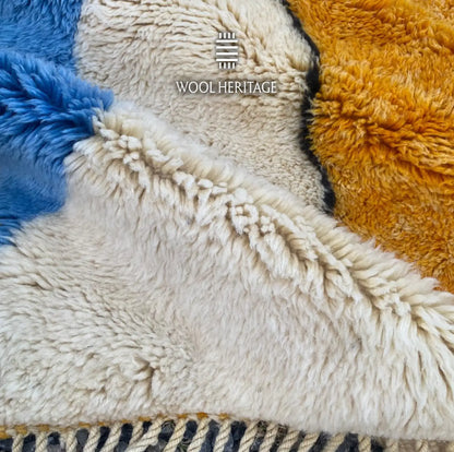 Detailed view of TAMURT rug showing blue, ivory, and ochre wool sections meeting beside the finished edge