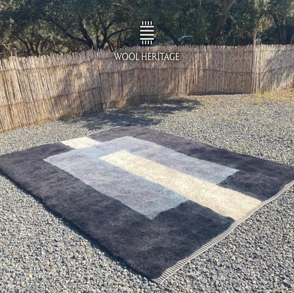 Angled view of TAWWURT Moroccan wool rug showing its navy field, pale blue portal, and central ivory passage