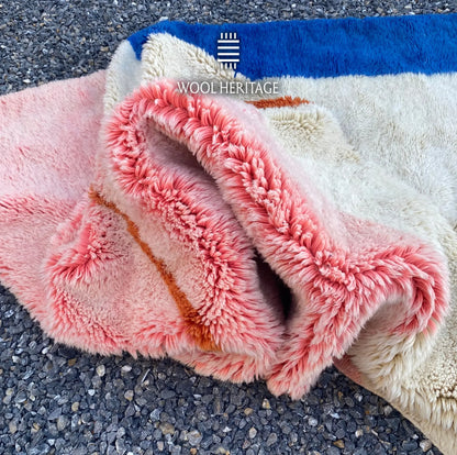 Folded detail of TAYRI rug showing its dense pink, ivory, and blue Moroccan wool pile