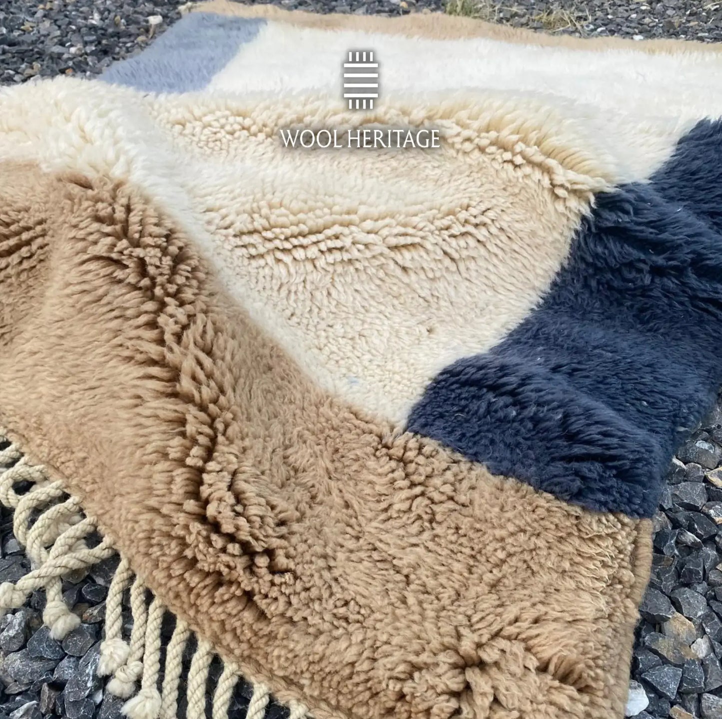 Folded detail of TIFAWT rug showing its beige, ivory, and deep-blue pile with hand-finished fringe