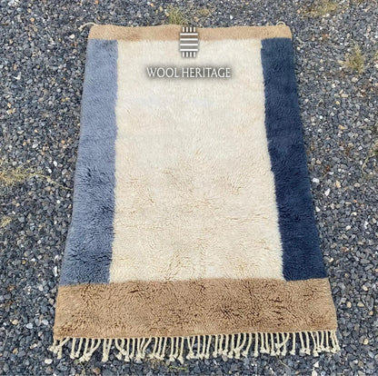 TIFAWT Beni Mrirt rug laid flat, showing its minimalist ivory center and asymmetrical blue borders
