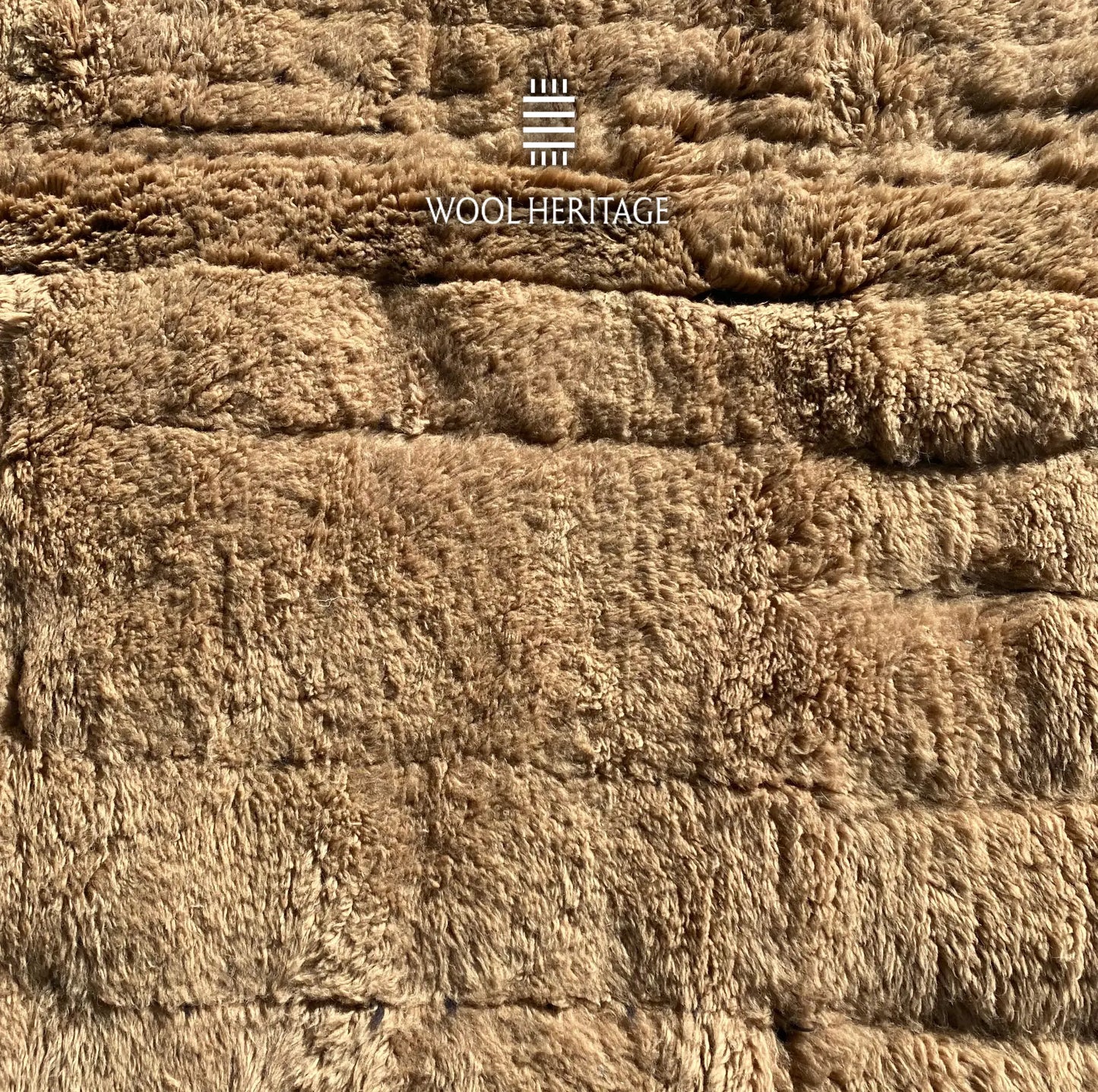 Close-up of TIRRA rug showing abstract raised forms and recessed markings across the wool pile