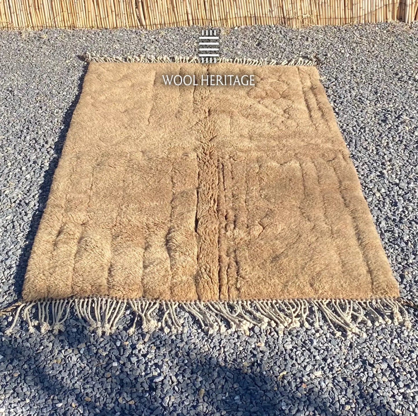 TIRRA golden-brown wool rug laid flat, showing its asymmetrical carved lines and relief forms