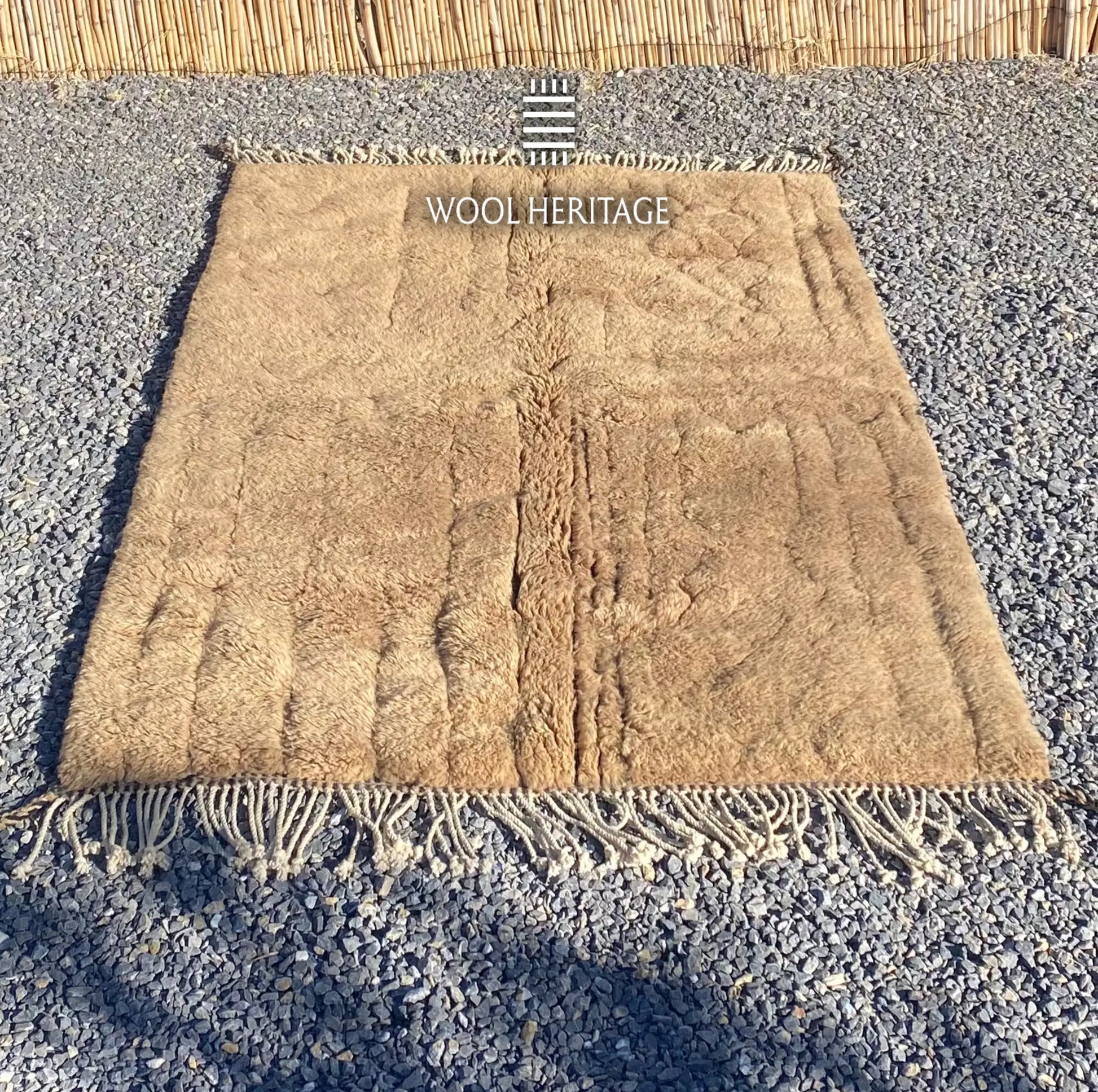 TIRRA golden-brown wool rug laid flat, showing its asymmetrical carved lines and relief forms
